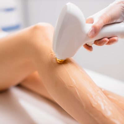 close-up woman's perfect legs while getting hair removal procedure in salon. professional beautician or cosmetologist use special ointment and apparatus. soft and smooth hairless skin on legs